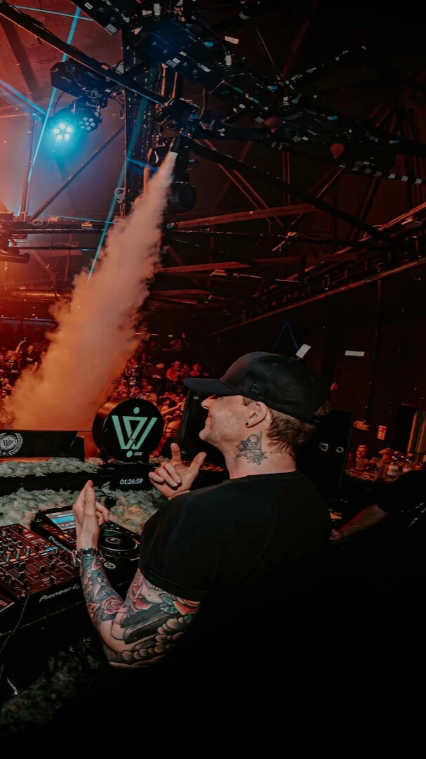 Niels Van Gogh is standing behind a DJ Booth while looking at the crowd and dancing.