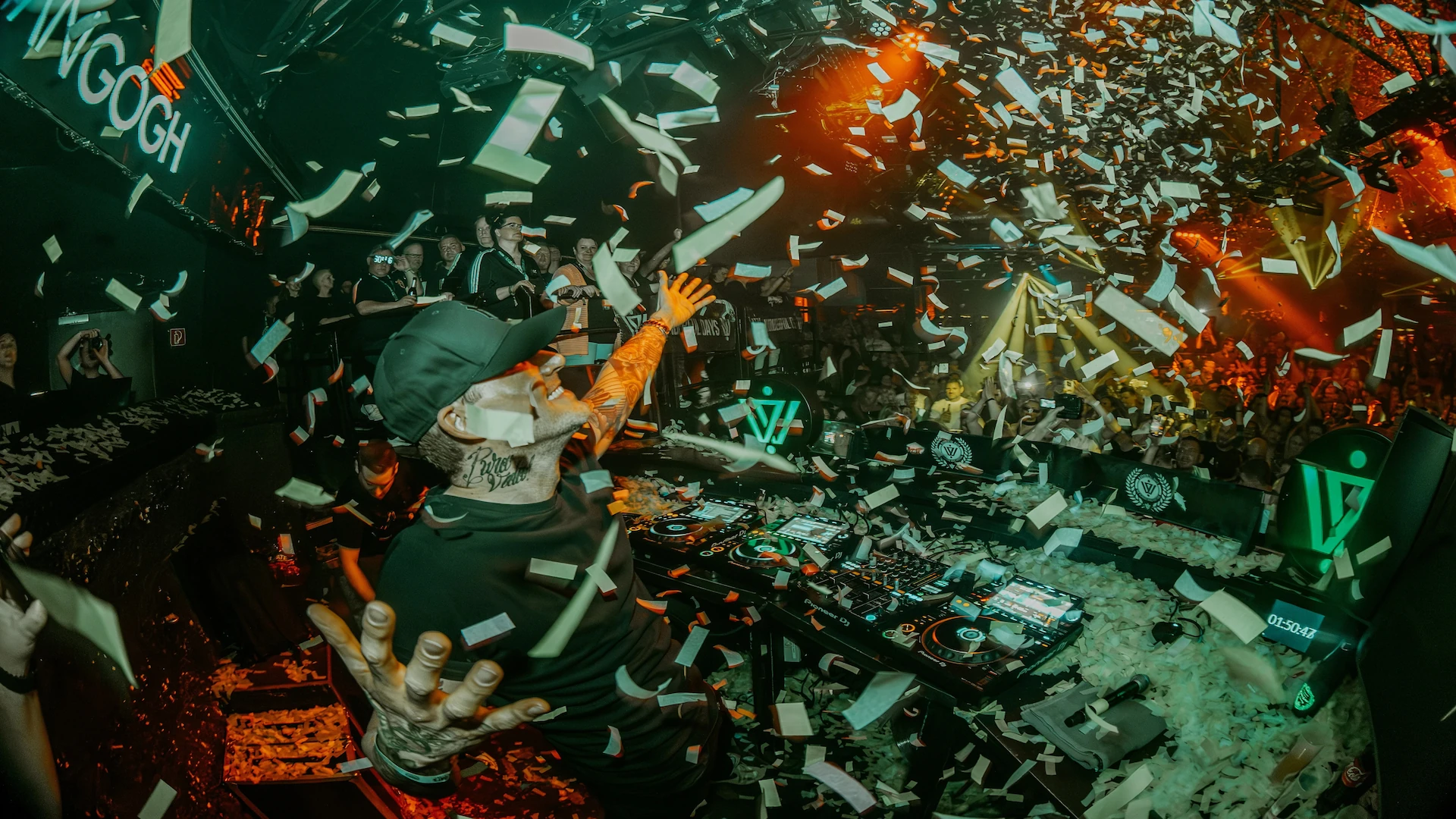 Niels Van Gogh is standing behind a DJ booth in front of a crowd while it is raining confetti.