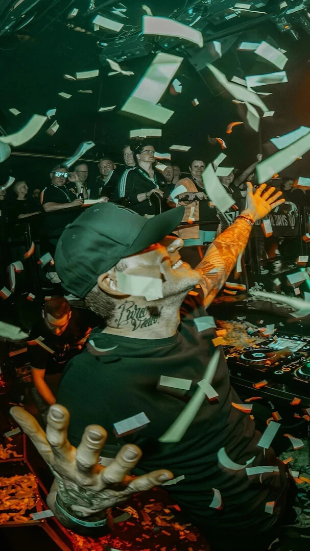 Niels Van Gogh is standing behind a DJ booth in front of a crowd while it is raining confetti.